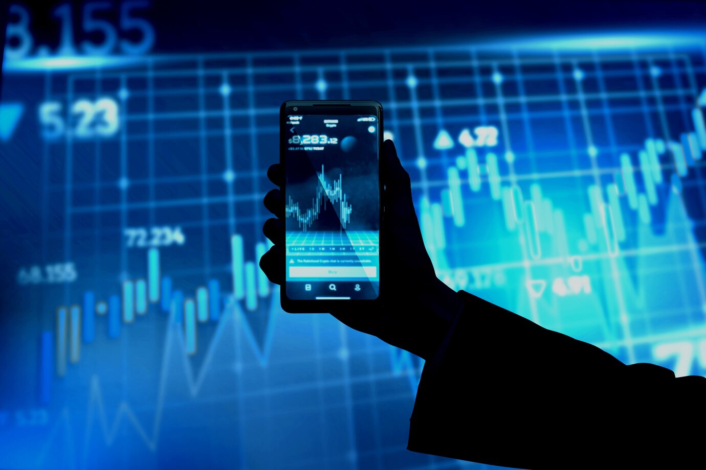 A hand holds up a smartphone displaying a stock market graph, with a large blue digital screen in the background highlighting financial charts and fluctuating numbers—perfect imagery for bold marketing strategies or Highrisk Marketing.