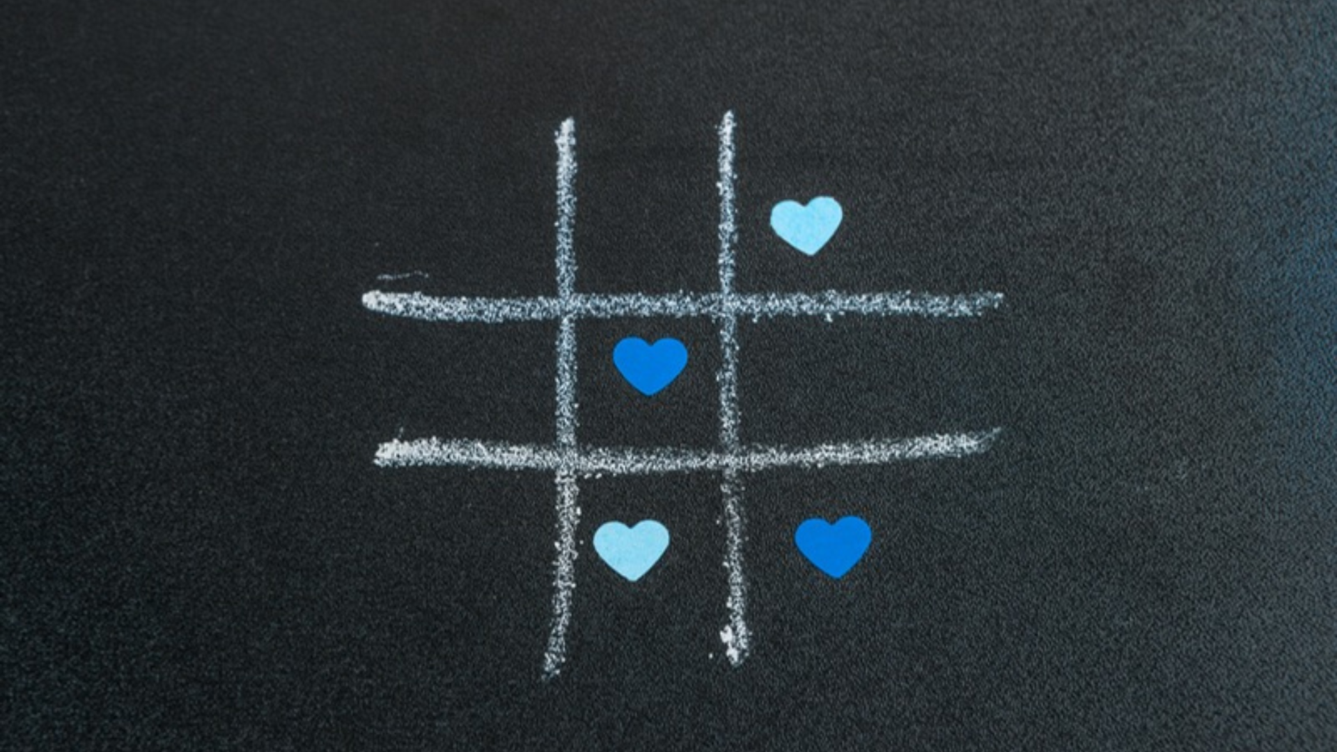 A chalk-drawn hashtag symbol on a blackboard with blue and light blue heart icons placed inside the grid, symbolizing the connection between love, social media, and trending hashtags.